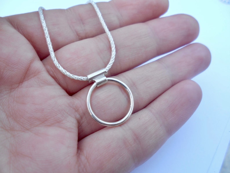 Pode incluir: Um colar de tom prateado com uma corrente fina e texturizada, ligada a um pendente circular liso. O pendente est&aacute; preso &agrave; corrente por uma pequena argola met&aacute;lica retangular, criando um design simples e limpo para esta pe&ccedil;a de joalharia.