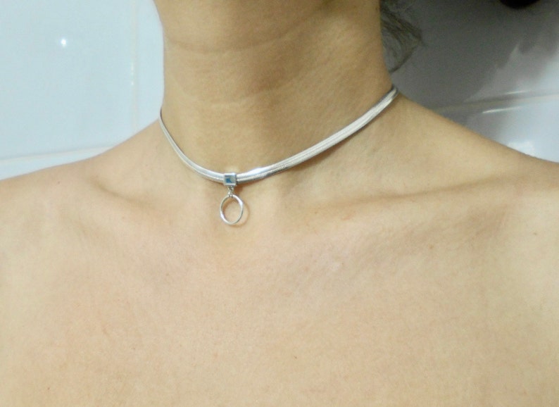 K&ouml;nnte beinhalten: Eine silberne Choker-Kette mit einem kleinen, runden Anh&auml;nger.