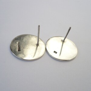 May include: A pair of silver earrings with a round shape. The back of the earrings are marked with "FIZARRIE" and "925".