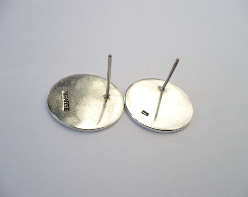 May include: A pair of silver earrings with a round shape. The back of the earrings are marked with "FIZARRIE" and "925".