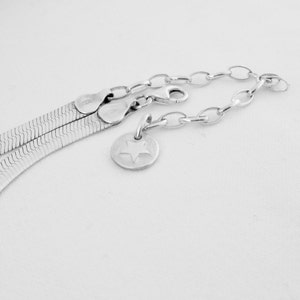 May include: A silver chain necklace with a silver star charm. The chain is a herringbone style and has a lobster clasp.
