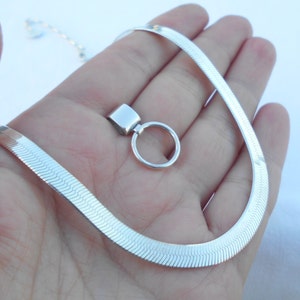 May include: A silver snake chain necklace with a silver pendant. The pendant is a small circle with a square attached to it.