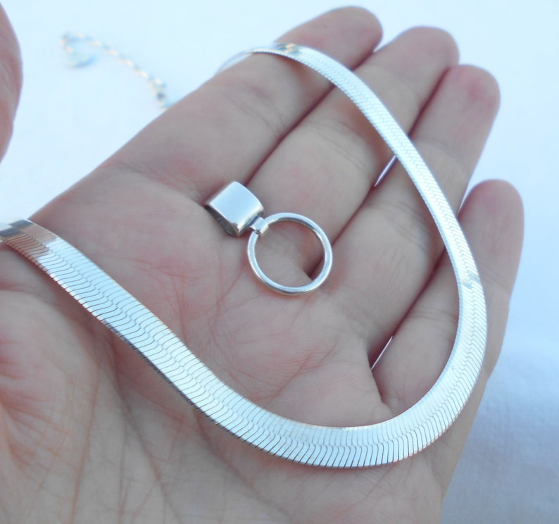 May include: A silver snake chain necklace with a silver pendant. The pendant is a small circle with a square attached to it.