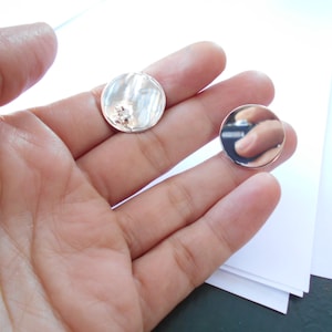 May include: Two silver round earrings, one with a textured surface and a small clear stone, the other smooth and reflective.