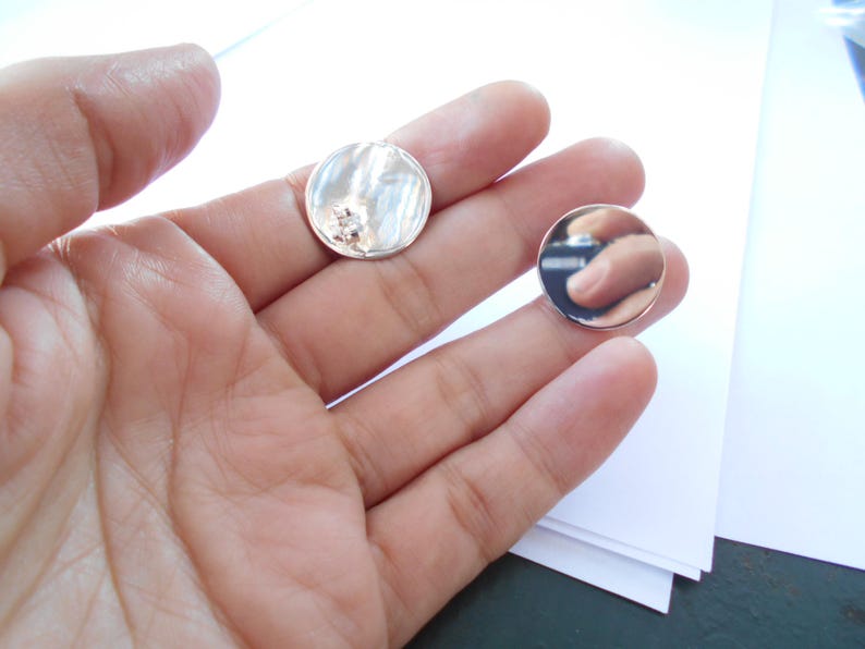 May include: Two silver round earrings, one with a textured surface and a small clear stone, the other smooth and reflective.