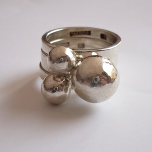 May include: A silver ring with three round, textured spheres attached to the band. The ring is made of three bands stacked on top of each other.
