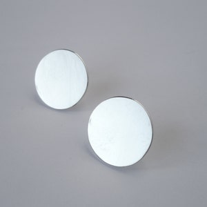 May include: A pair of silver circular stud earrings. The earrings are smooth and have a shiny finish.