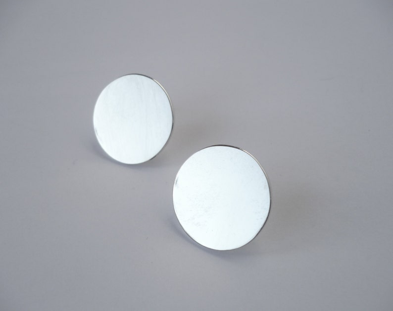 May include: A pair of silver circular stud earrings. The earrings are smooth and have a shiny finish.