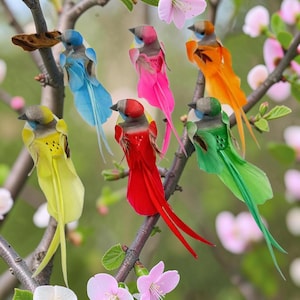 Op de afbeelding: Een verzameling kleurrijke kunstvogels met gevederde vleugels en staarten. De vogels zitten op boomtakken, met een verscheidenheid aan kleuren, waaronder geel, blauw, roze, rood, oranje en groen. De achtergrond toont roze bloemen.
