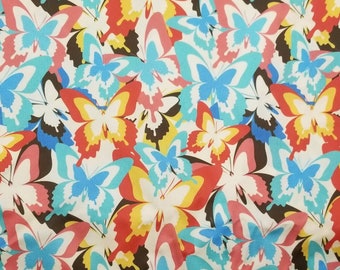 May include: A textile featuring a repeating pattern of butterflies in various colours. The butterflies are in shades of blue, red, yellow, and pink, set against a cream background. The design is a vibrant and eye-catching fabric.
