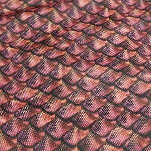 May include: Close-up of a fabric with a textured pattern resembling scales. The scales are a mix of red, purple, and gold colours.