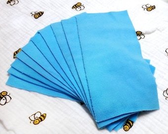May include: A stack of ten light blue fabric squares, folded in a fan shape, on a white background with a pattern of black and yellow bees.