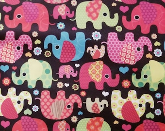 May include: A colourful fabric with a repeating pattern of pink, green, blue and yellow elephants with polka dots and floral designs. The background is black.