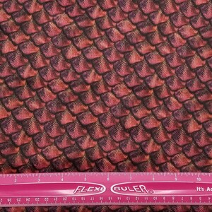 May include: Red and black fabric with a dragon scale pattern. The fabric is measured with a pink ruler.