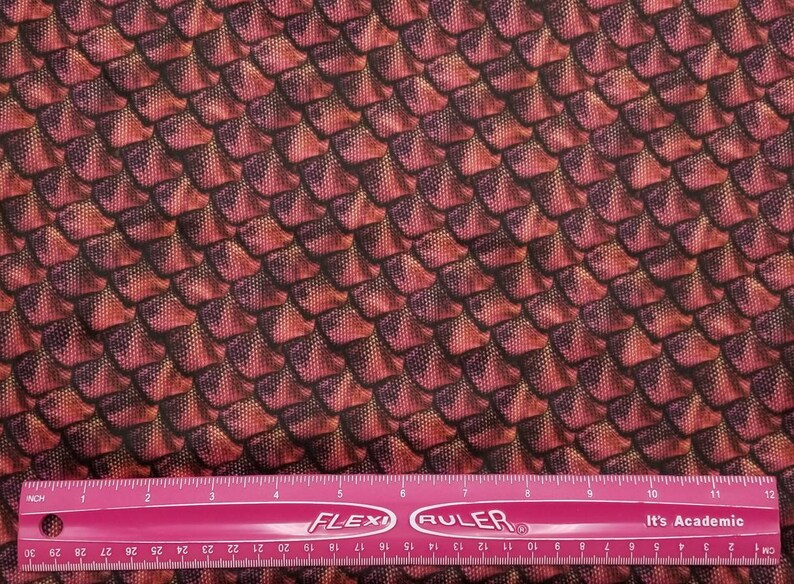 May include: Red and black fabric with a dragon scale pattern. The fabric is measured with a pink ruler.
