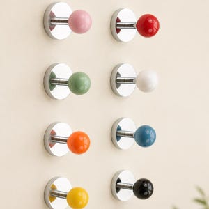 May include: A collection of eight wall-mounted coat hooks. Each hook features a polished chrome disc base and a colorful, spherical knob. Colors include pink, red, green, white, orange, blue, yellow, and black.