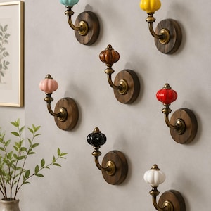 May include: A collection of decorative wall hooks with colorful ceramic knobs. Each hook features a different colored knob, including blue, yellow, pink, brown, red, black, and white, mounted on a round wooden base with a brass hook.