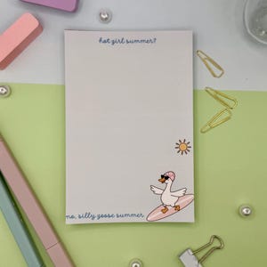 May include: A rectangular notepad with a white background featuring the text hot girl summer? at the top and no, silly goose summer at the bottom. A small yellow sun and a cartoon goose wearing sunglasses and a pink hat on a surfboard are included.