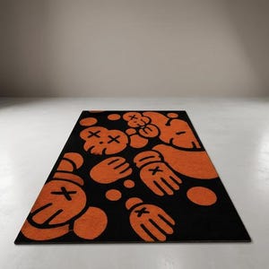 Pu&ograve; includere: Un tappeto rettangolare caratterizzato da un motivo ripetuto di mani guantate in stile cartone animato e teste di personaggi con occhi a forma di X arancioni su uno sfondo nero. Il design include diversi punti circolari arancioni sparsi.