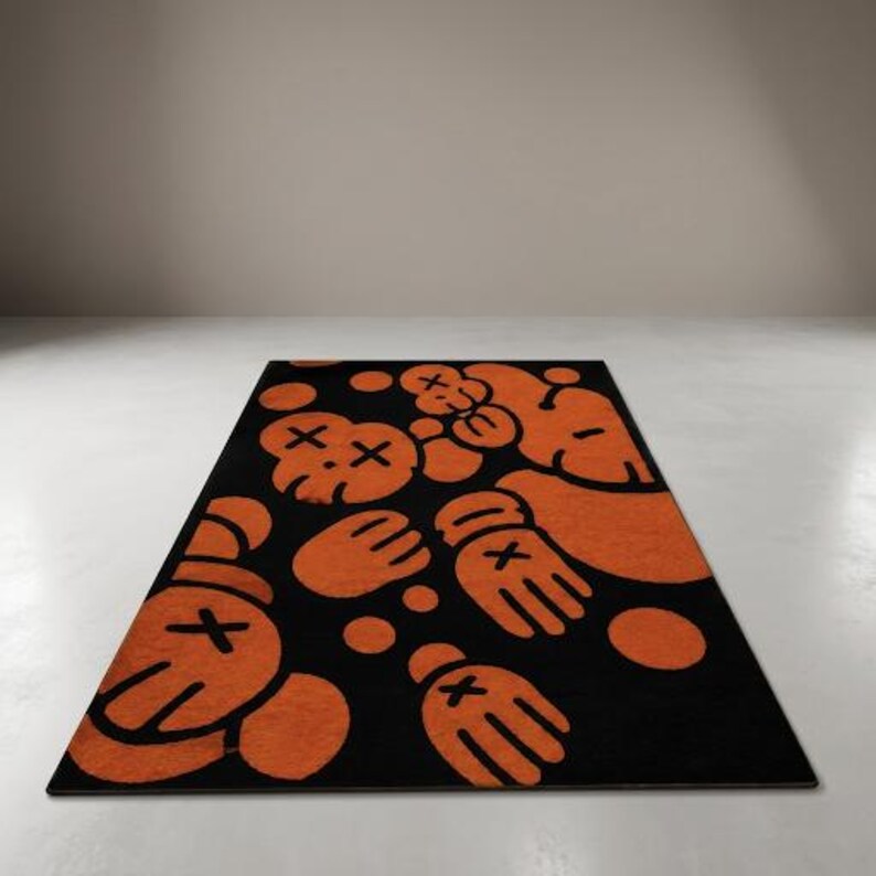 Pu&ograve; includere: Un tappeto rettangolare caratterizzato da un motivo ripetuto di mani guantate in stile cartone animato e teste di personaggi con occhi a forma di X arancioni su uno sfondo nero. Il design include diversi punti circolari arancioni sparsi.