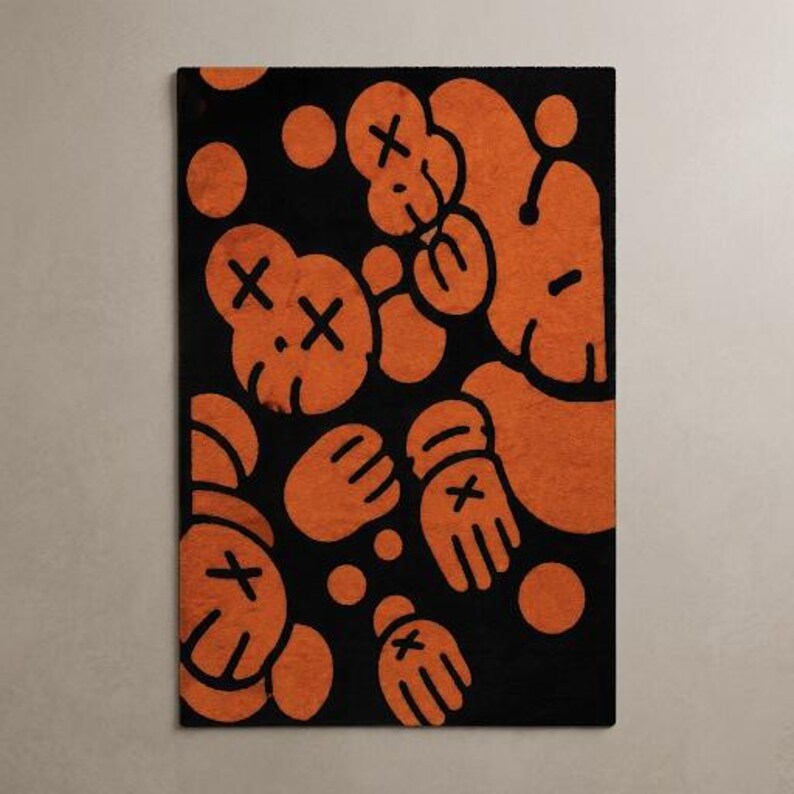 Pu&ograve; includere: Un tappeto rettangolare con sfondo nero e un motivo grafico arancione ripetuto. Il design &egrave; composto da teste e mani stilizzate in stile cartone animato, ciascuna contrassegnata da una X sugli occhi e sui palmi, intervallate da cerchi arancioni.