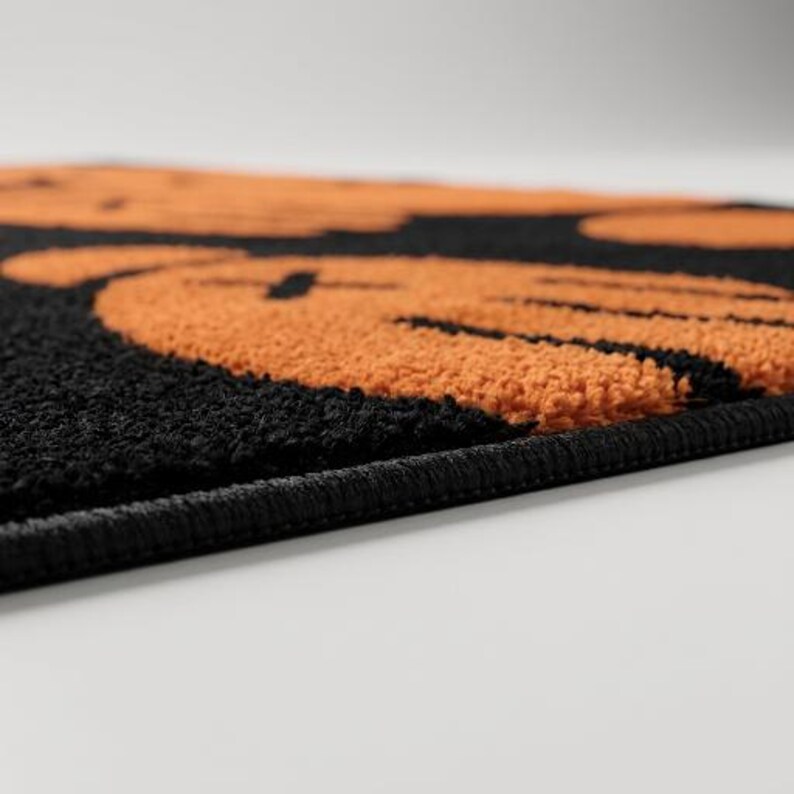 Pu&ograve; includere: Un tappeto rettangolare con sfondo nero e un motivo ripetuto di facce circolari arancioni in stile cartone animato. Ogni faccia presenta due occhi a forma di X e una semplice linea curva per la bocca. Il tappeto ha una consistenza trapuntata.