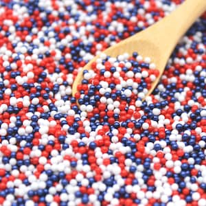 May include: A close-up of red, white, and blue sprinkles in a bowl. A wooden spoon is partially submerged in the sprinkles.