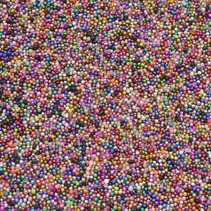 May include: A close-up view of a dense collection of small, colorful beads. The beads display a variety of colors, including pink, purple, green, gold, and black, creating a vibrant and textured surface. The beads are uniform in size and shape.