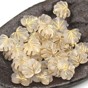 May include: A collection of clear glass leaf-shaped beads with gold accents. The beads are scattered on a brown surface.