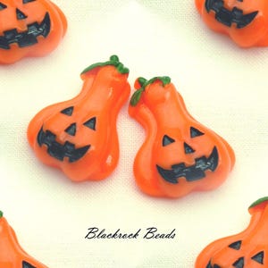 May include: A collection of orange pumpkin-shaped beads with black carved facial features and green stems. Each bead displays a smiling jack-o'-lantern expression. The text Blackrock Beads is printed in black in the center of the image.
