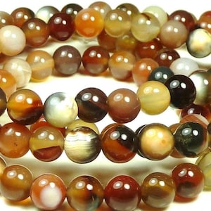 May include: Strands of round gemstone beads in shades of brown, amber, and cream. The beads have a polished, glossy finish and vary in color and pattern. These beads are suitable for jewelry making.