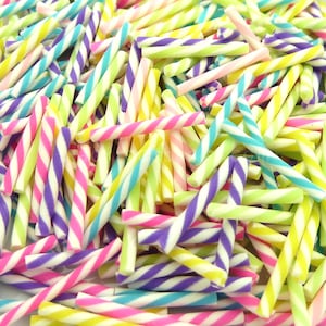 May include: A close-up shot of a pile of colorful, twisted polymer clay canes. The canes are in various colors, including pink, purple, yellow, green, and blue, with white stripes. These decorative canes are used for nail art and other craft projects.