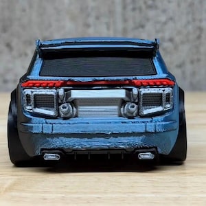 Può includere: Un'auto giocattolo blu metallizzato vista dal retro, dotata di spoiler nero, luci posteriori orizzontali rosse, griglia posteriore argentata e doppio scarico integrato nel paraurti inferiore. Presenta ampi passaruota neri.