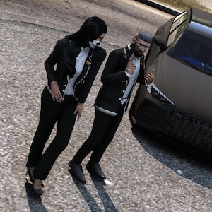 May include: Two figures stand beside a matte black saloon car. One figure wears a black blazer over a white shirt and black trousers. The other figure wears a black blazer with white trim over a white shirt and black trousers. The car has a dark grille.