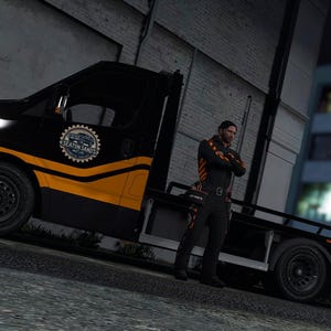 May include: A black and orange flatbed tow truck featuring a circular logo on the door with the text Seaton Sands. The vehicle has a low-profile cab, black steel wheels, and a long rear bed designed for vehicle transport, parked on a paved surface.