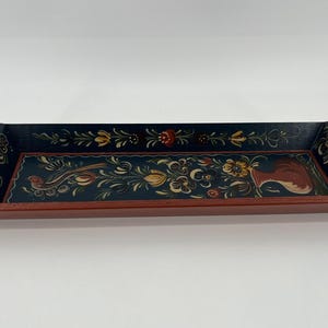May include: A rectangular wooden tray with a red base and black interior. The tray features a hand-painted floral design with a rooster and bird. The handles have heart-shaped cutouts. The tray is approximately 16 inches long.