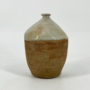 May include: A handcrafted ceramic vase with a textured, brown lower half and a smooth, off-white upper portion. The vase has a rounded body and a narrow neck, showcasing a rustic aesthetic. The pottery is likely handmade.
