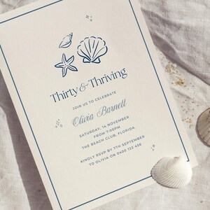 Könnte beinhalten: Eine cremefarbene Einladung mit blauem Rand und dem Text "Thirty & Thriving". Das Design umfasst Illustrationen von Muscheln, Seesternen und Muscheln. Die Einladung enthält auch den Namen "Olivia Barnett" und Veranstaltungsdetails.