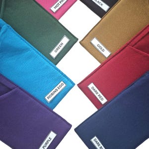 May include: A collection of eight rectangular fabric pouches in various solid colors, each featuring a white rectangular label with black text identifying the color: Hot Pink, Black, Green, Gold, Robins Egg, Dark Red, Purple, and Dark Blue.