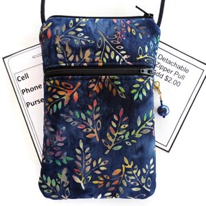 May include: A small blue crossbody bag with a zipper closure and a colorful floral pattern. The bag has a detachable zipper pull, which is an optional add-on for $2.00. The bag is designed to hold a cell phone, purse, and other small items.
