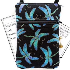 May include: Black crossbody purse with a dragonfly print. The purse has two zippered compartments and a detachable zipper pull.  "Plus Size"  "Cell Phone Purse" is written on a white card behind the purse.  "Detachable Zipper Pull add $2.00" is written on a white card to the right of the purse.