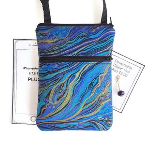 May include: A small blue and gold crossbody bag with a zipper closure. The bag has a black adjustable strap and a detachable zipper pull. The bag is made of a fabric with a marbled pattern.