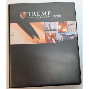 May include: A black binder with the text "TRUMP UNIVERSITY" and "WEALTH IN REAL ESTATE" printed on the front. The binder features a collage of images, including a pen, a laptop, and a house.