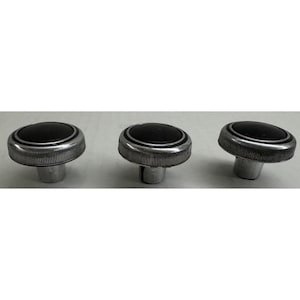 Op de afbeelding: Drie knoppen in vintage-stijl met een zwart midden, zilveren rand en een geribbelde, zilveren basis. Deze knoppen zijn waarschijnlijk voor een auto of een ander mechanisch apparaat.