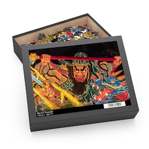 May include: A 120-piece 8x10 puzzle in a black box featuring a vibrant, illuminated Japanese festival float design. The image depicts a fierce, bearded warrior figure holding a red staff, accompanied by a blue dragon with glowing eyes and sharp teeth.