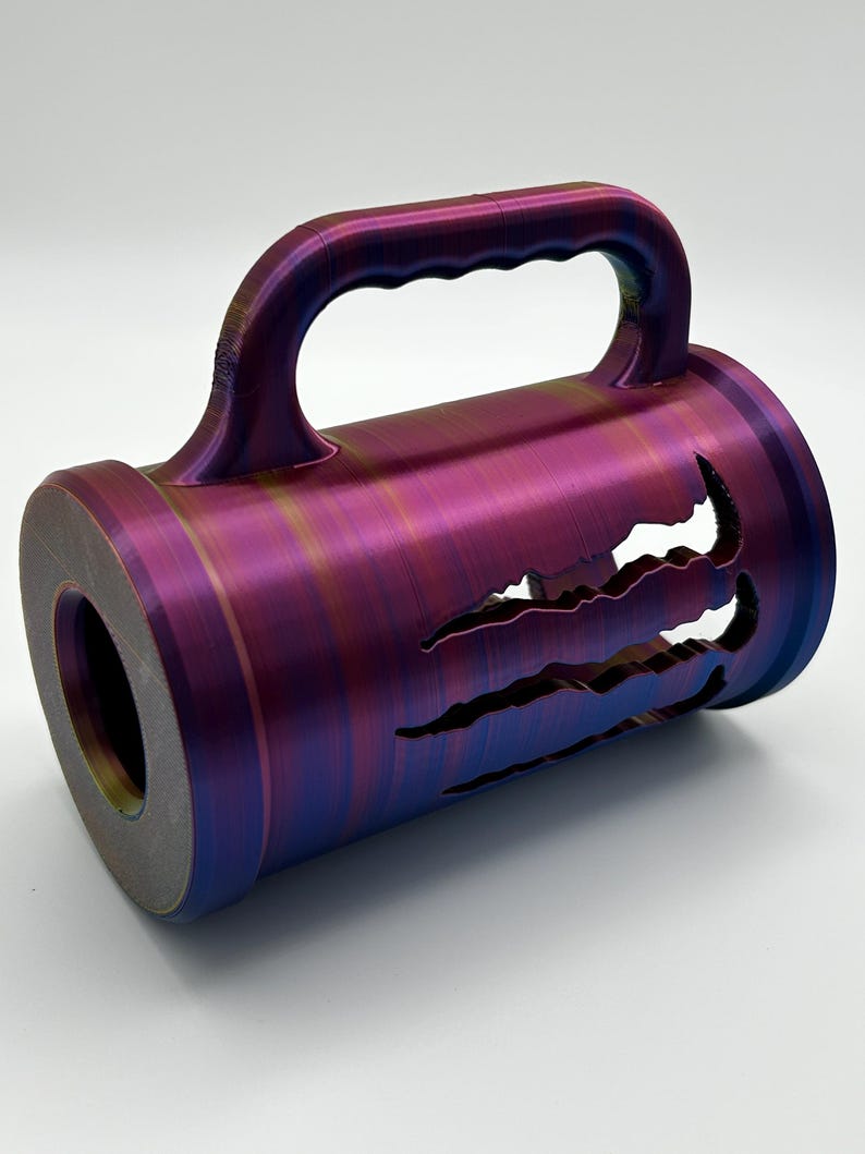 May include: A cylindrical object with a handle, featuring a color-shifting finish of purple, blue, and gold. The design includes claw-shaped cutouts along the side. The object has a circular opening on one end.