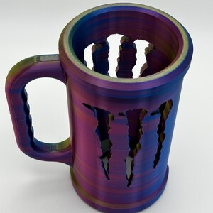 May include: A multi-colored, iridescent mug with a handle. The mug features a design of claw marks cut out of the side. The mug is made of a hard plastic material and is suitable for beverages.