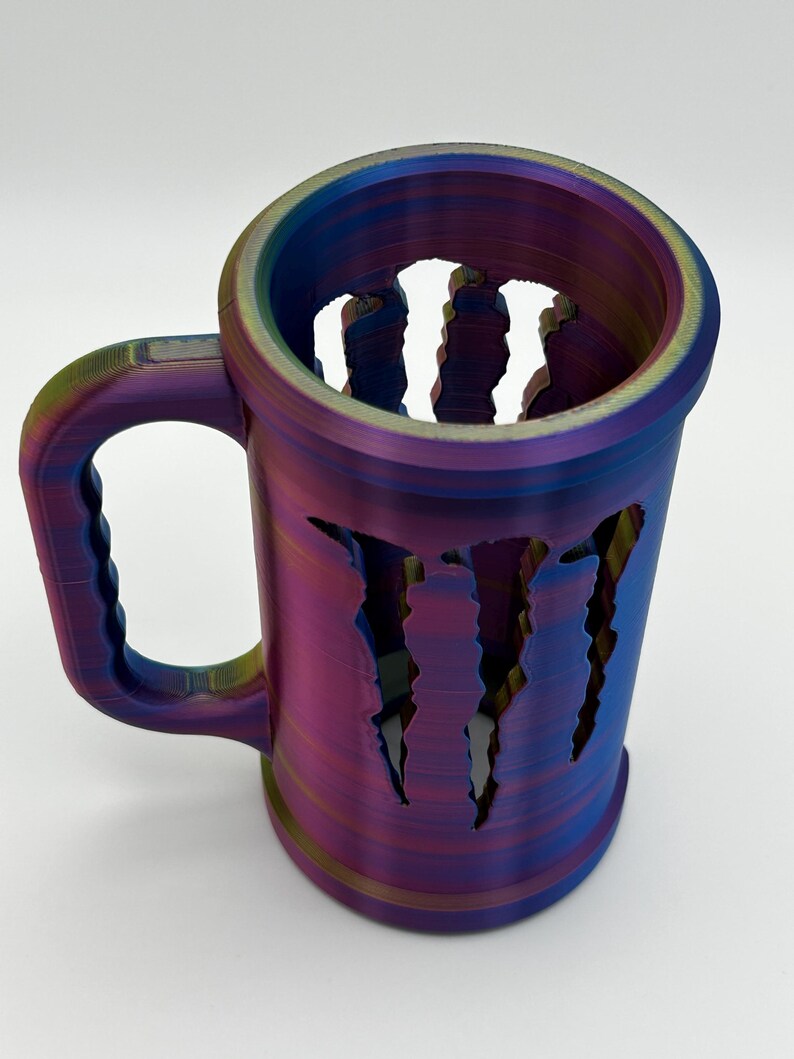May include: A multi-colored, iridescent mug with a handle. The mug features a design of claw marks cut out of the side. The mug is made of a hard plastic material and is suitable for beverages.