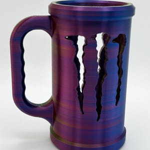 May include: A cylindrical mug with a large handle, featuring a color-shifting finish of purple, blue, and gold. The mug has three vertical, jagged cutouts on the side. The mug is designed to hold beverages.