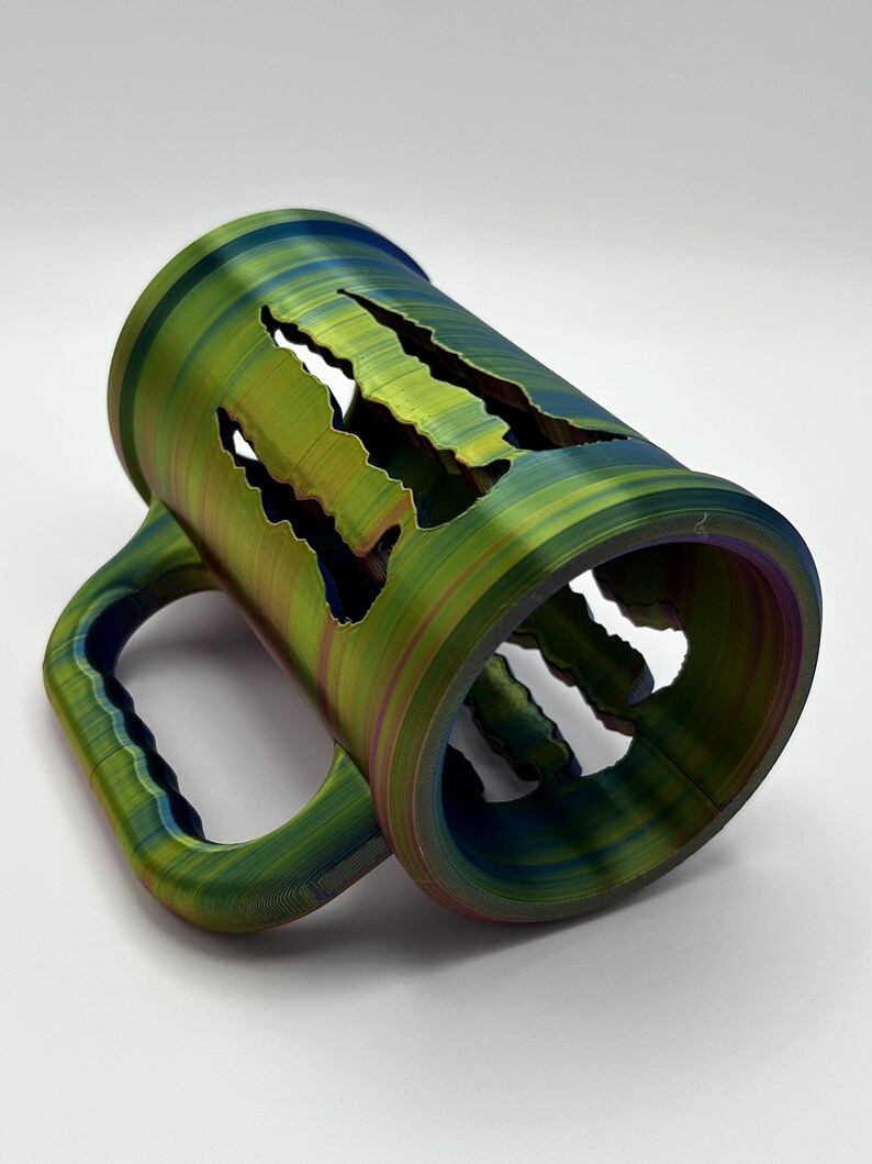 May include: A multi-colored mug with a unique design. The mug features a green, blue, and purple color scheme with a handle and cut-out claw marks. The mug is made of a durable material and is suitable for hot or cold beverages.